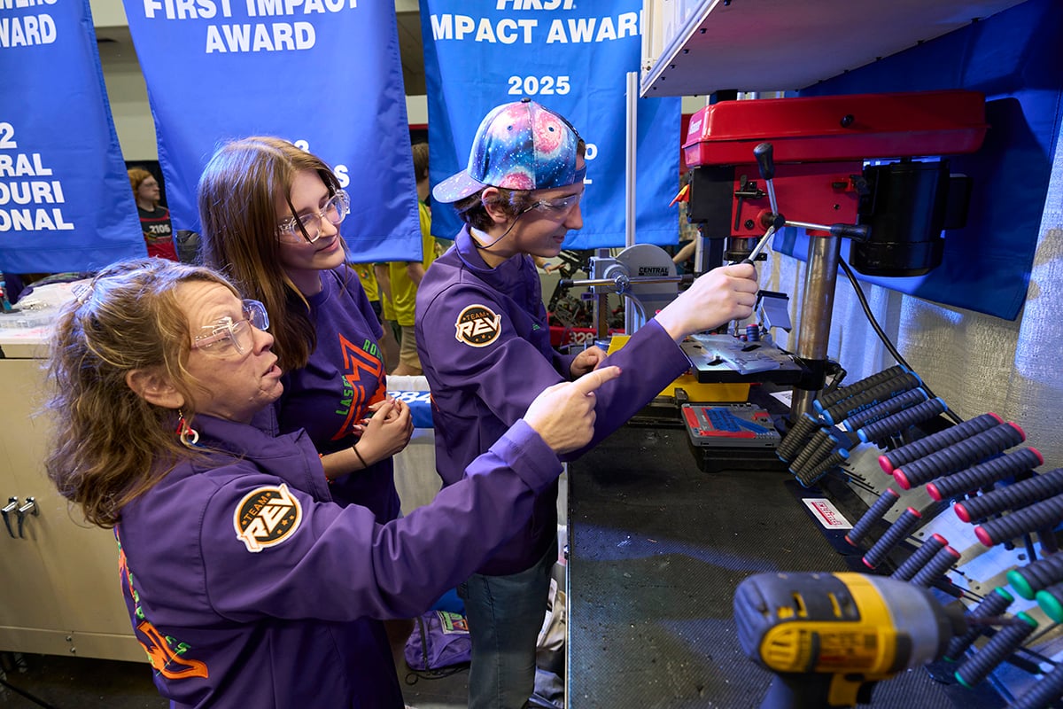 Two FIRST Robotics Competition students working on their robot at FIRST Championship with the help of a FIRST mentor.